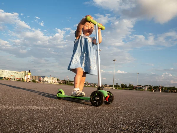 Straat Sport: Gelukkig meisje in het berijden van een scooter kick op de stoep en plassen. — Stockfoto