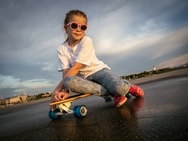 Street sports: Jolly Girl in sunglasses sat down to relax on the longboard after a walk in the park for skating.