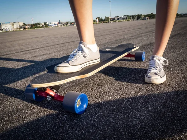 Straat snelle sport: een meisje in grijze sneakers is rollen op een longboard langs de weg. Asfalt is besmeurd met snelheid. — Stockfoto