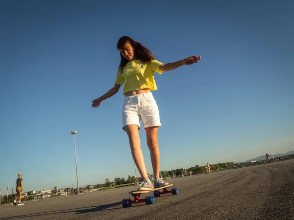 Street Sports: A girl in a bright yellow T-shirt is rolling on a longboard on the citys asphalt.