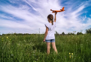 Bir kız bebek bir oyuncak iskeleti planör bir mavi gökyüzü arka plan bulutlar ile bir alanda başlatıyor.