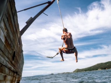 Cliff atlama: şortlu genç bir adam deniz suyu eski bir gemi yan atlar..