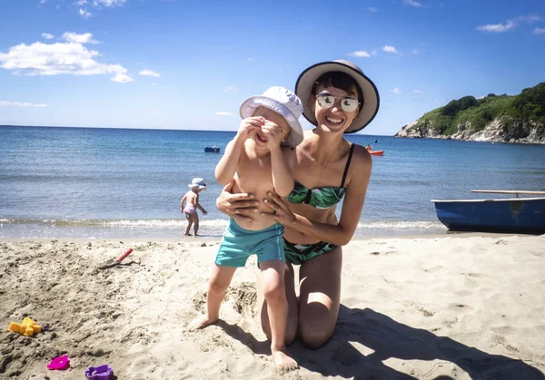 Отдых на море: моя мама в солнечных очках и шляпа отдыхает с ребенком на песчаном пляже. Крупный план . — стоковое фото