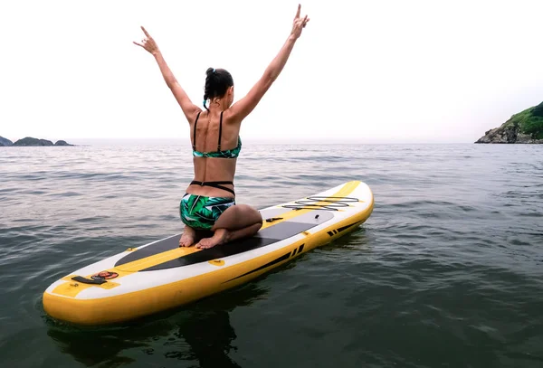 Férias no mar: a menina navega em um sup-board amarelo e em ondas do mar e alegremente levanta as mãos para o topo . — Fotografia de Stock