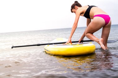 Bir kız bir mayo bir sap tahta üzerinde bir raket denizde su bendi kapağı.