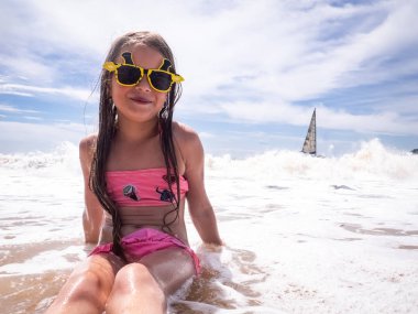 Denizde tatil: okul öncesi bir kız komik güneş gözlüğü kıyı dalgalar, sahilinde oturur.