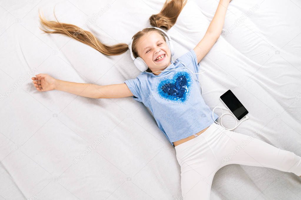 Music lover: The girl stretches out on a big white bed and listens to music in big white headphones.