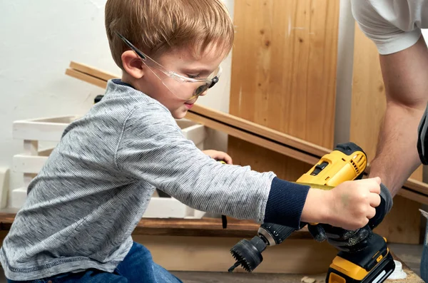 Family time: Dad shows his son hand tools, a yellow screwdriver and a hacksaw. They need to drill and drill boards for repair.