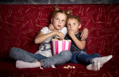 Çocuk sinema: bir kız ve bir erkek evde karanlıkta büyük bir kırmızı koltuk üzerinde bir film izlemek ve patlamış mısır yemek. Portre.