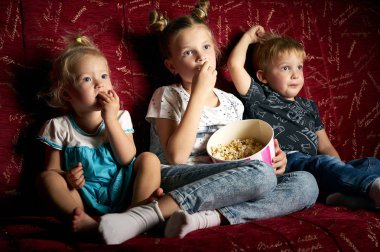 Çocuk filmleri: üç çocuk içinde belgili tanımlık karanlık büyük bir kırmızı kanepede evde film izlemek ve patlamış mısır yemek.