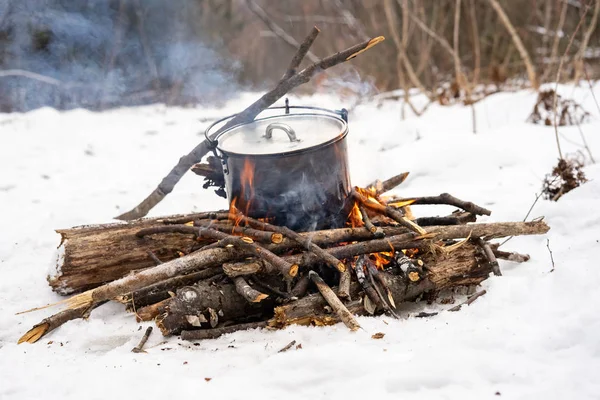 Winter hike: a small bonfire in the forest and a pot on the fire.