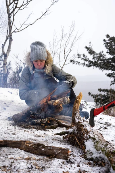 Yürüyüş: A durmak üstünde gri şapkalı bir kız kendini ateşin yanında kışın dağlarda ısınıyor.
