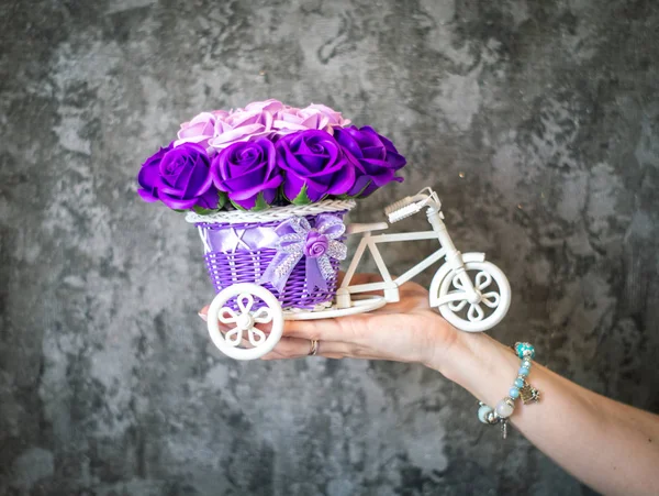 Decoración floral festiva: una pequeña cesta decorativa en forma de tenedor con capullos de flores púrpuras sobre un fondo gris . — Foto de Stock