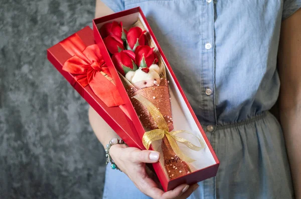 Floristas trabajan: Una chica demuestra una caja con un ramo de rosas rojas y un oso de peluche . — Foto de Stock