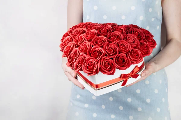 Flores como regalo: Una niña sostiene un gran ramo de rosas rojas en una caja blanca sobre un fondo blanco . —  Fotos de Stock