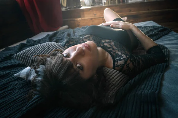 Uma menina com grandes olhos em um vestido preto está deitada em uma cama cinza escuro de cabeça para baixo. Aparência bonita e relaxamento . — Fotografia de Stock