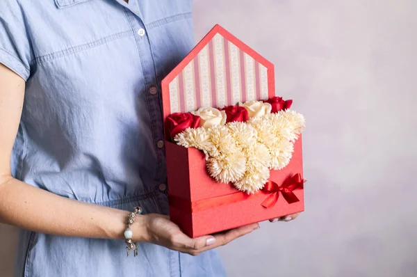 Flores como regalo: Una niña en un vestido azul presenta un sobre rojo vintage con una caja de flores . — Foto de Stock