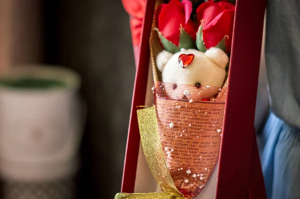 Floristas trabajan: Una chica demuestra una caja con un ramo de rosas rojas y un oso de peluche . — Foto de Stock