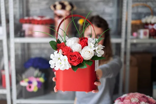Un ramo de rosas blancas y rojas en una caja roja en las manos extendidas de la florista . — Foto de Stock