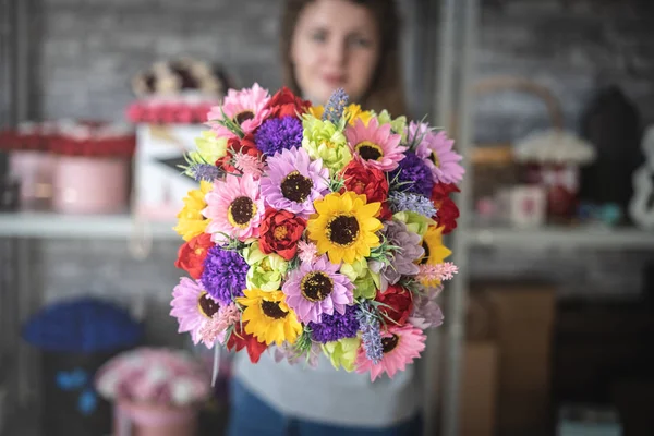 Una chica tiene un ramo de flores de colores. Las flores están en foco, el resto es borroso . — Foto de Stock