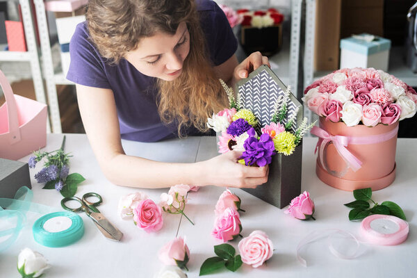 Flower workshop: a girl florist assembles a bouquet of colorful flowers to order in a purple envelope box.