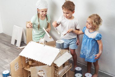 Çocuklar yetişkin olarak: bir erkek ve bir kız bir oyuncak ev beyaz boya ve boya ile kirli olsun. Otantik fotoğraf.