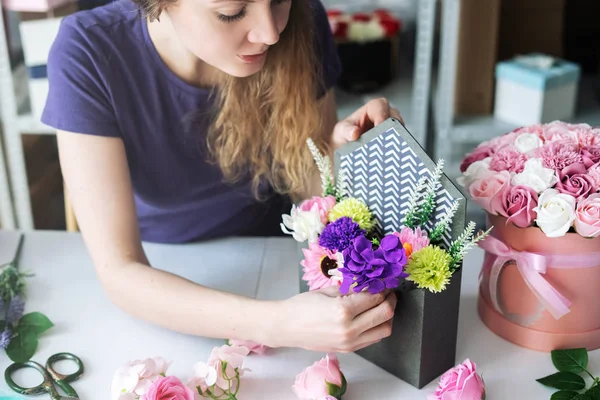 Flower workshop: a girl florist assembles a bouquet of colorful flowers to order in a purple envelope box.
