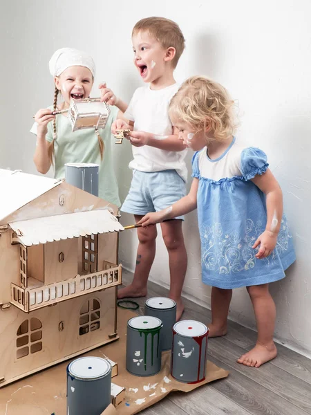 Дети как взрослые: Мальчик и девочка красят кукольный домик в белый цвет и запачкаются краской. Аутентичное фото . — стоковое фото