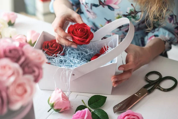 Floristería: floristería recoge un ramo de rosas rojas en una canasta de papel azul . — Foto de Stock