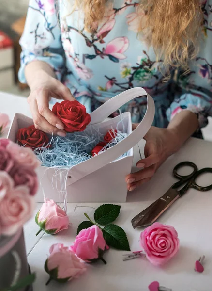 Floristería: floristería recoge un ramo de rosas rojas en una canasta de papel azul . — Foto de Stock