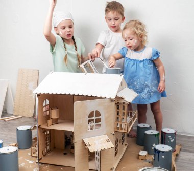 Çocuklar yetişkin olarak: bir erkek ve bir kız bir oyuncak ev beyaz boya ve boya ile kirli olsun. Otantik fotoğraf.