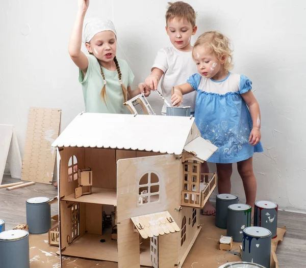 Crianças como adultos: Um menino e uma menina pintam uma casa de boneca de branco e sujam com tinta. Foto autêntica . — Fotografia de Stock