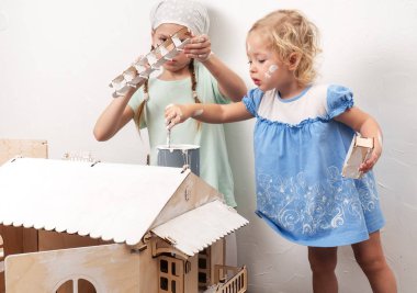 Çocuk iş başında: iki kız kardeş boya beyaz bez bebek evin çatısı. Genç kız, dikkatle smear boya yapar.