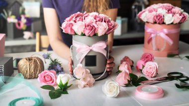Flower shop: bir çiçekçi kız bir buket pembe gül yuvarlak bir kutu içinde toplar. Sarı Kıvırcık saçlı, gri arka plan.
