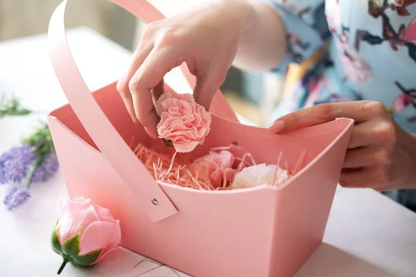 Floristería recoge un ramo de rosas rosadas y claveles en una canasta de papel rosa . — Foto de Stock
