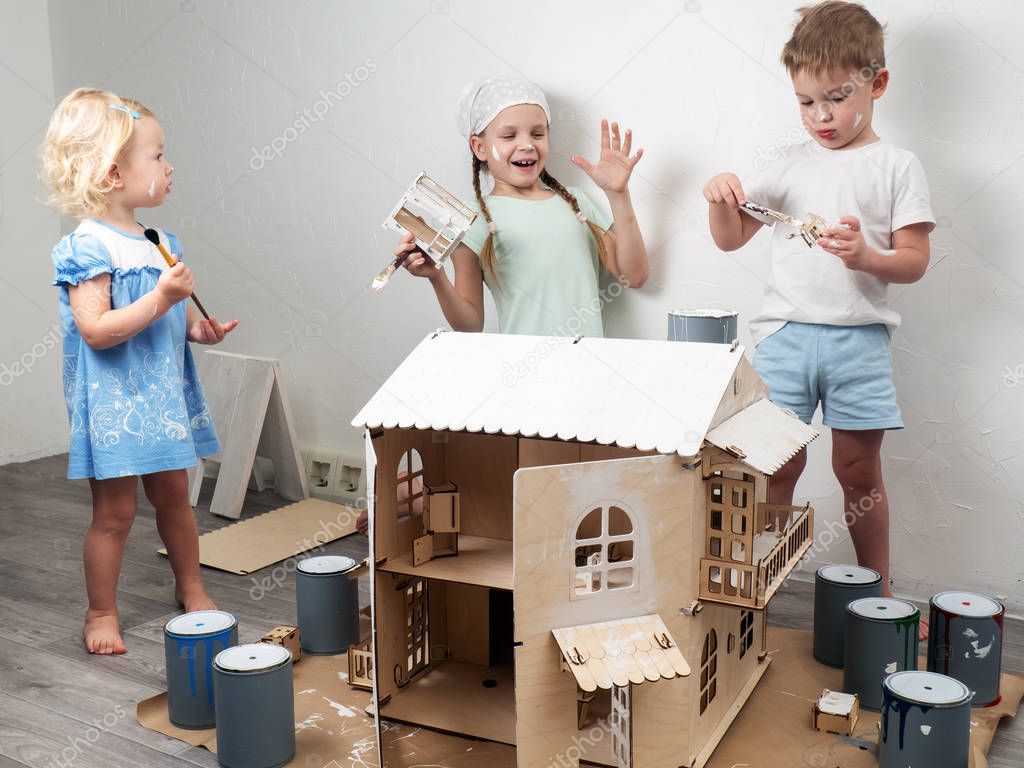 Children as adults: A boy and a girl paint a doll house white and get dirty with paint. Authentic photo.