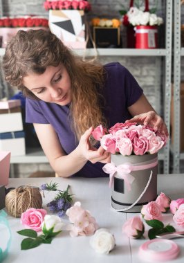 Flower shop: bir çiçekçi kız bir buket pembe gül yuvarlak bir kutu içinde toplar. Sarı Kıvırcık saçlı, gri arka plan.