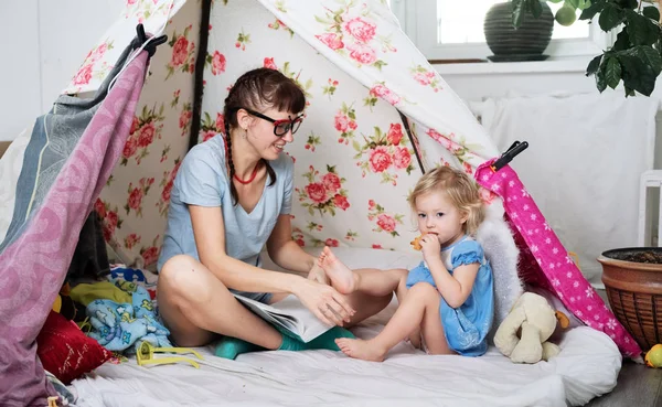 Tempo em família: mamãe e algumas das irmãs crianças brincam em casa em uma tenda caseira para crianças . — Fotografia de Stock