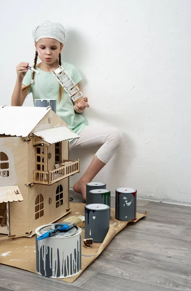 Crianças no trabalho: A menina claramente pinta a fachada da casa de boneca com um pequeno borla em branco . — Fotografia de Stock