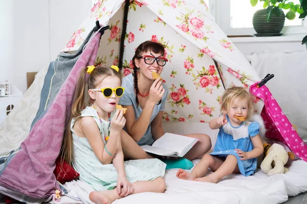 Tempo em família: mamãe e algumas das irmãs crianças brincam em casa em uma tenda caseira para crianças . — Fotografia de Stock