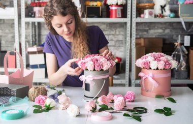 Flower shop: bir çiçekçi kız bir buket pembe gül yuvarlak bir kutu içinde toplar. Sarı Kıvırcık saçlı, gri arka plan.