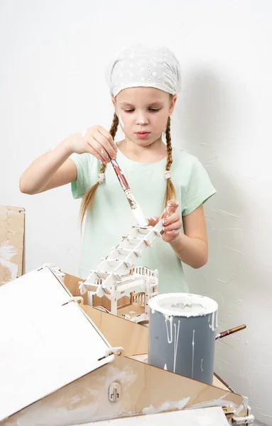 Дети за работой: Девушка аккуратно красит фасад кукольного домика небольшим кисточкой в белом . — стоковое фото