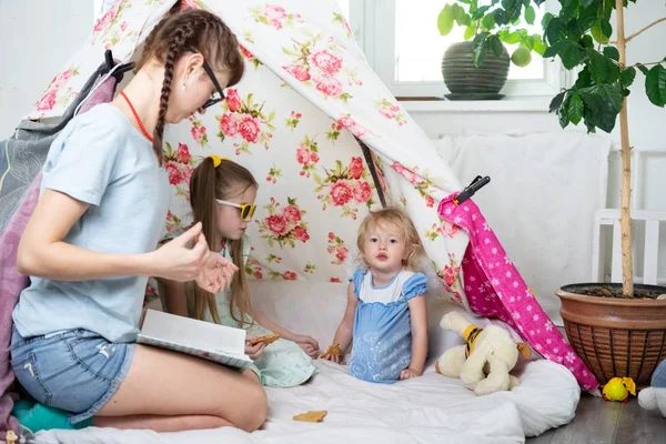 Tempo em família: mamãe e algumas das irmãs crianças brincam em casa em uma tenda caseira para crianças . — Fotografia de Stock