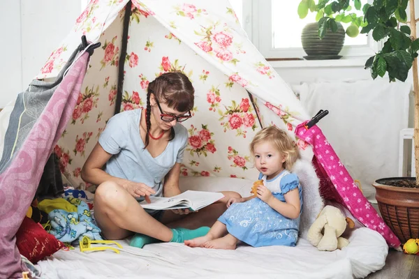 Tempo em família: mamãe e algumas das irmãs crianças brincam em casa em uma tenda caseira para crianças . — Fotografia de Stock