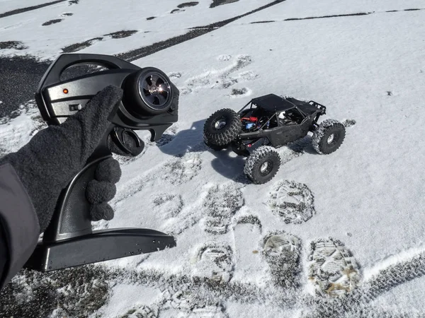 Radio controlled car models: a small black buggy in the snow and a control controller in the hand of a person. Bright bright picture. — Stock Photo, Image