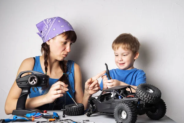 Mulheres no trabalho dos homens: Mãe ajuda seu filho com a fixação de um modelo de buggy controlado por rádio . — Fotografia de Stock