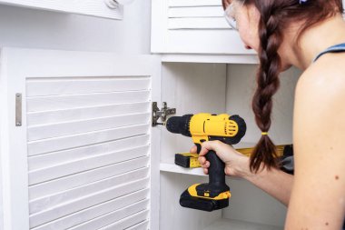 Kız erkek meslekler: mavi giysili bir kadın beyaz bir kabine kapı mobilya menteşeleri kilitleniyor. Yakın çekim. Kopya alanı