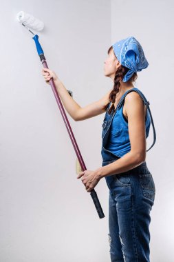 Mavi giysili kızı onarım yapar ve duvarlar beyaz bir rulo ile boyar.