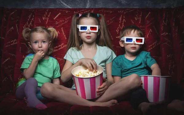 Cinéma pour enfants : les enfants s'assoient sur un canapé rouge et regardent un film en 3D . — Photo