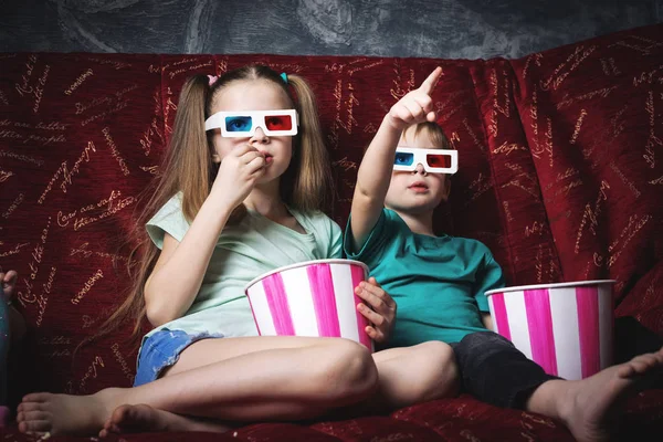 Childrens cinema: Children sit on a red sofa and watch a 3D movie. — Stock Photo, Image